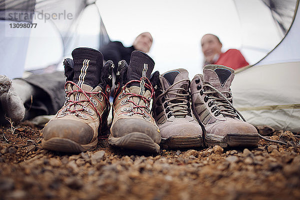 Nahaufnahme von schmutzigen Schuhen mit Wanderern  die sich im Hintergrund entspannen