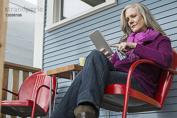 Niedriger Blickwinkel auf eine Frau beim Online-Shopping  die auf einem Stuhl auf der Veranda sitzt