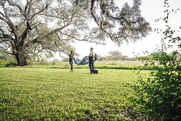 Ehepaar legt Decke auf Grasfeld gegen den Himmel im Park
