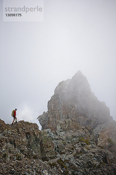 Hochwinkelaufnahme eines Wanderers mit Rucksack  der auf einem Berg inmitten von Wolken steht