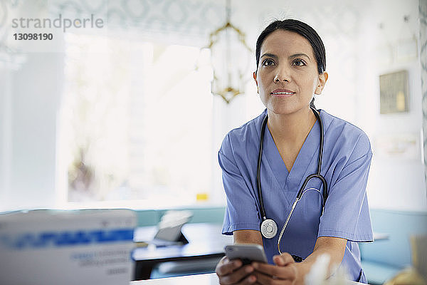 Ärztin schaut weg  während sie im Krankenhaus ein Smartphone in der Hand hält