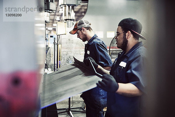 Seitenansicht von Arbeitern  die mit Stahlblech an Maschinen in der Industrie arbeiten