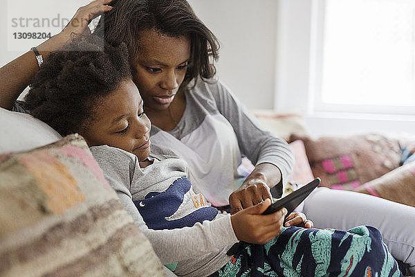 Mutter und Sohn benutzen Tablet-Computer  während sie sich zu Hause auf dem Sofa entspannen