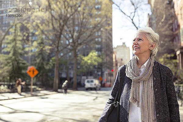 Nachdenkliche ältere Frau lächelt auf der Straße in der Stadt