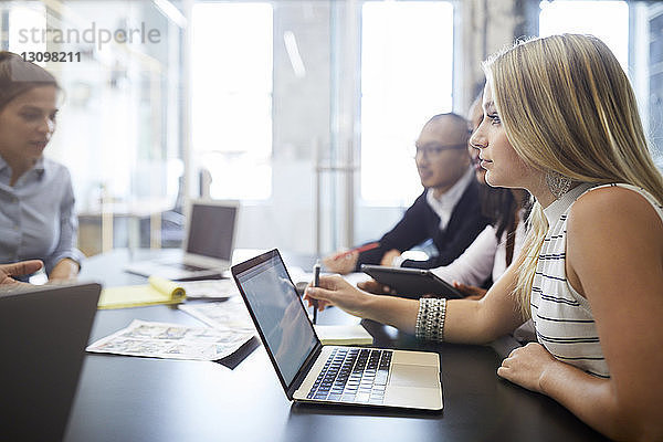 Geschäftsfrau benutzt Laptop  während sie mit Kollegen während einer Besprechung am Konferenztisch sitzt