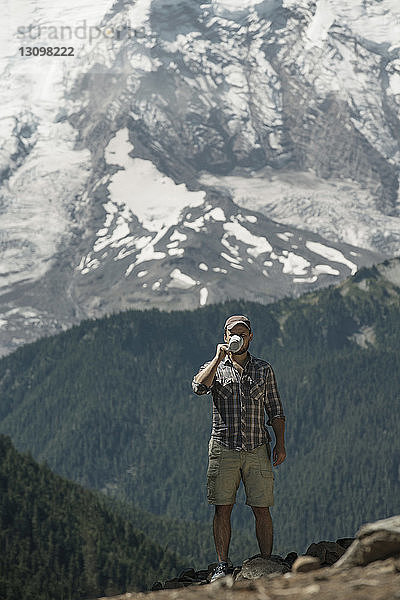 Mann trinkt Kaffee  während er auf Felsen gegen Berge steht