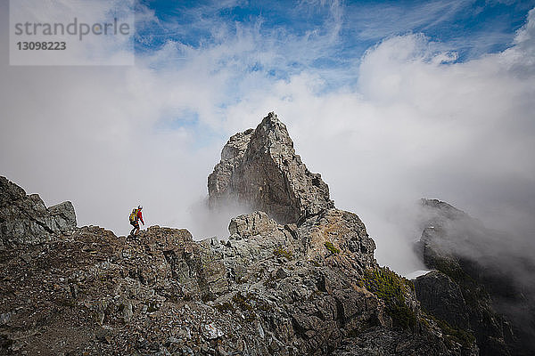Hochwinkelaufnahme eines Wanderers mit Rucksack auf einem Berg inmitten von Wolken