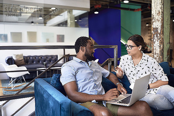 Multi-ethnische Geschäftsleute diskutieren über Laptop  während sie im Kreativbüro auf dem Sofa sitzen