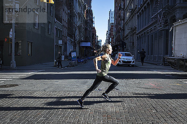 Seitenansicht einer Athletin  die an einem sonnigen Tag auf einer Straße in der Stadt läuft