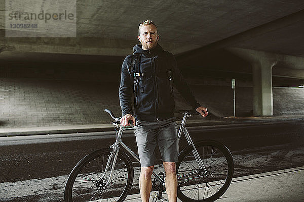 Porträt eines selbstbewussten männlichen Pendlers  der mit dem Fahrrad auf der Brücke steht