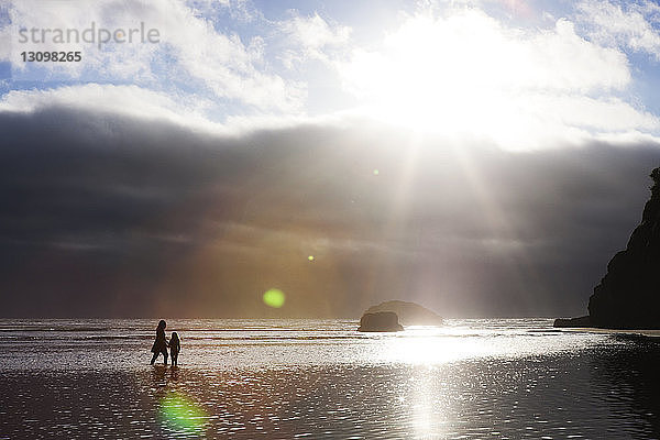 Mutter und Tochter gehen im Meer gegen bewölkten Himmel