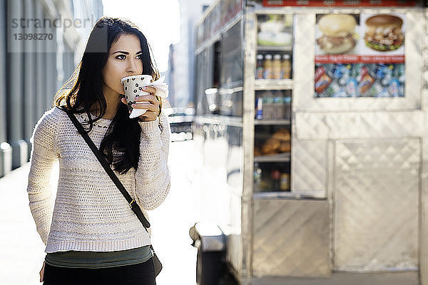 Junge Frau trinkt Kaffee aus Einwegglas mit Konzessionsstand im Hintergrund