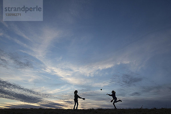 Scherenschnittschwestern spielen mit dem Ball auf dem Feld gegen den Himmel