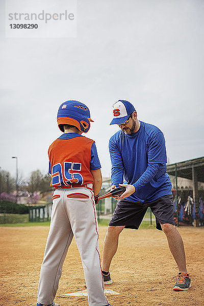 Trainer assistiert dem Jungen beim Baseballspielen auf dem Feld