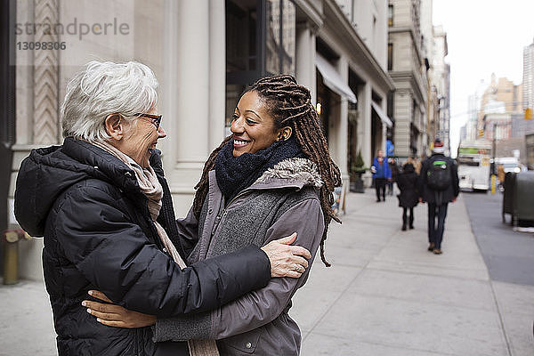 Glückliche Frauen umarmen sich  während sie auf der Straße stehen