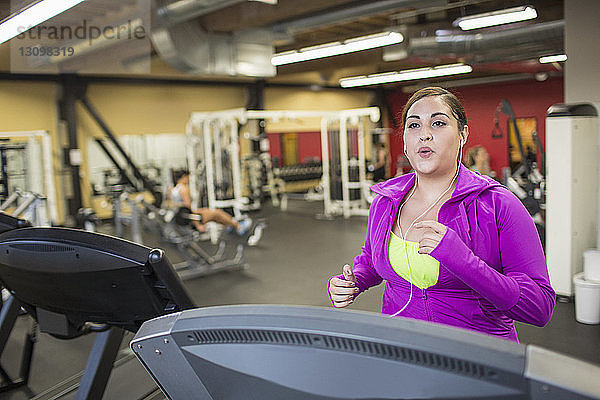 Frau hört Musik  während sie im Fitnessstudio auf dem Laufband trainiert