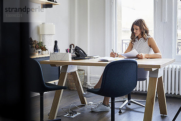 Geschäftsfrau  die mit Dokumenten arbeitet  während sie im Büro am Schreibtisch sitzt