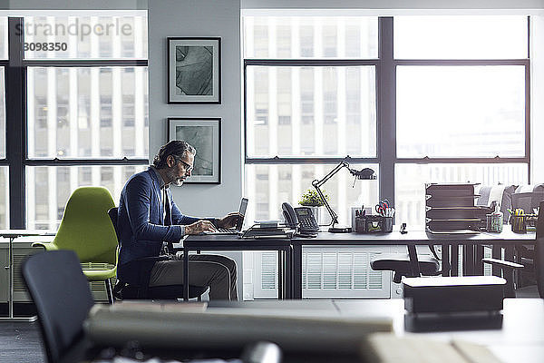 Geschäftsmann benutzt Laptop-Computer  während er im Büro gegen das Fenster arbeitet