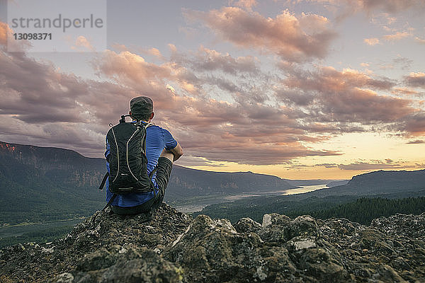 Rückansicht eines auf einem Berg sitzenden Wanderers mit Rucksack im Crater Lake National Park