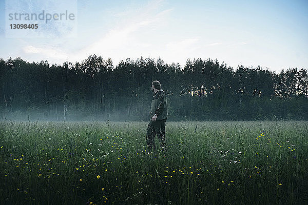 Seitenansicht eines Mannes  der bei nebligem Wetter auf einem Grasfeld gegen den Himmel steht