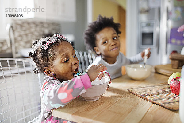 Mädchen isst Frühstücksflocken  während der Bruder sie in der Küche anschaut