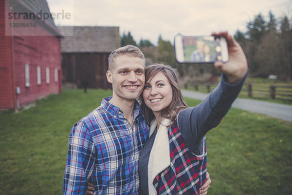 Glückliches Paar  das sich im Stehen auf einem Grasfeld ein Selfie nimmt