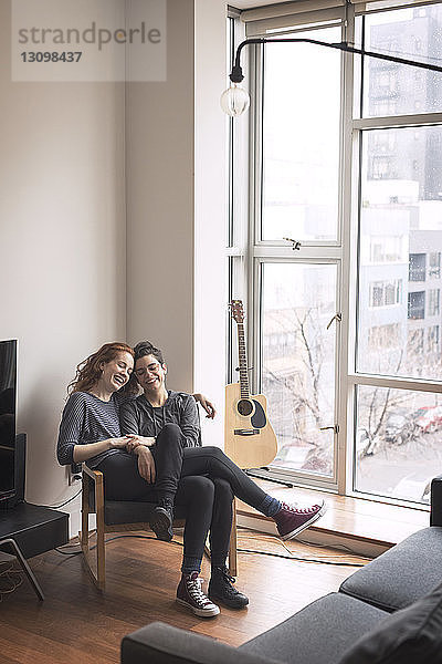Glückliches lesbisches Paar sitzt zu Hause auf einem Stuhl am Fenster