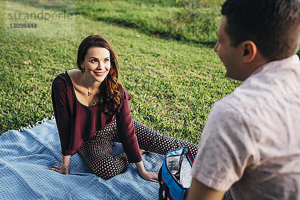 Hochwinkelaufnahme eines lächelnden Paares  das sich auf einer Decke im Park entspannt