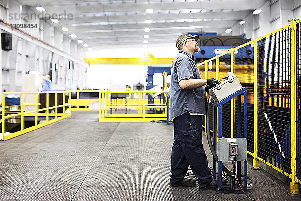 Arbeiter in voller Länge bei der Arbeit in einer Fabrik der Stahlindustrie an einer Kontrollmaschine