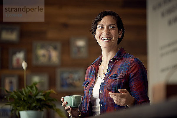 Niedrigwinkelansicht einer glücklichen Frau  die eine Kaffeetasse hält  während sie im Café steht