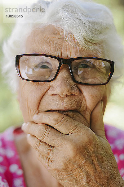 Nahaufnahme einer nachdenklichen älteren Frau mit Hand am Kinn  die eine Brille trägt