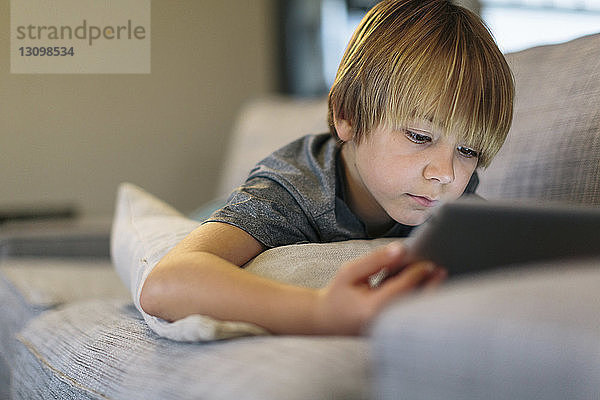 Nahaufnahme eines Jungen  der einen Tablet-Computer benutzt  während er zu Hause auf dem Sofa liegt