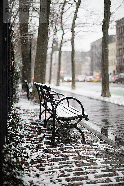 Schneebedeckte Bank am Bürgersteig in der Stadt