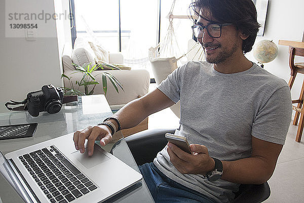 Hochwinkelansicht eines lächelnden Mannes mit Laptop bei der Arbeit zu Hause