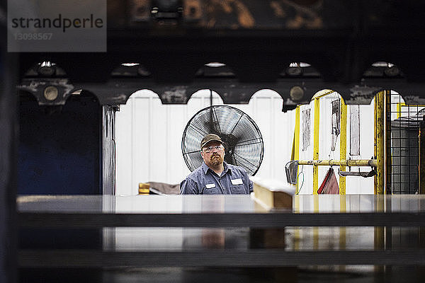 Porträt eines Arbeiters  der in einer Fabrik der Stahlindustrie gegen Bleche steht