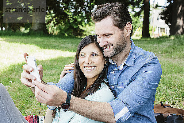 Glückliches Paar  das im Park sitzend Selbsthilfe per Handy nimmt