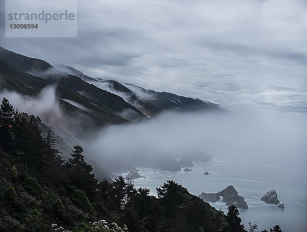 Hoher Winkel idyllischer Blick auf Berge am Meer gegen bewölkten Himmel bei Nebelwetter