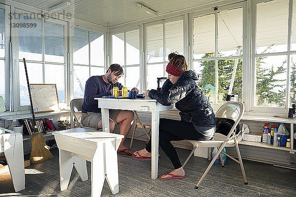 Paar liest Buch  während es in einer Hütte am Tisch sitzt