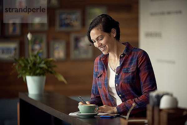 Lächelnde Frau schreibt  während sie im Cafe steht