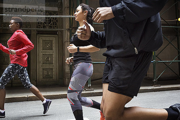 Seitenansicht von entschlossenen Athleten  die auf der Straße der Stadt joggen