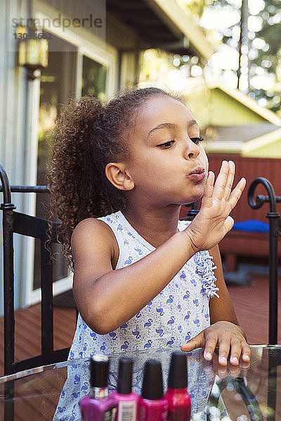 Mädchen bläst Nagellack auf Fingernägel  während sie im Hof am Tisch sitzt