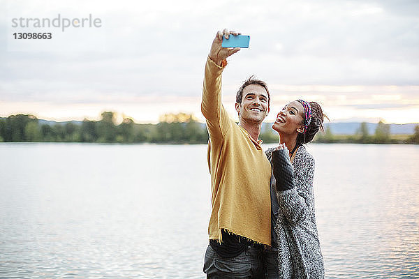 Freunde nehmen Selfie  während sie am Fluss gegen den Himmel stehen
