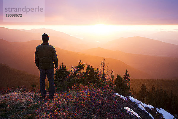 Rückansicht eines Wanderers  der bei Sonnenuntergang auf einem Berg steht