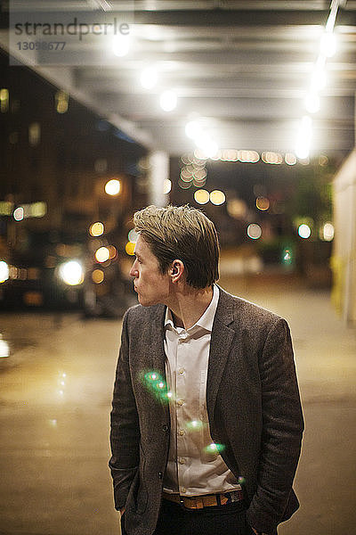 Mann in formaler Kleidung steht nachts auf beleuchtetem Bürgersteig