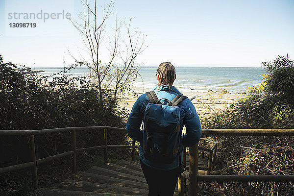 Rückansicht einer Frau mit Rucksack auf Stufen am Strand gegen den Himmel
