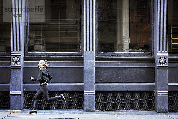 Seitenansicht einer Athletin  die auf einem Fußweg durch ein Gebäude in der Stadt läuft