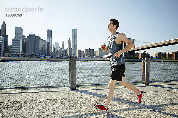 Seitenansicht eines Mannes  der auf dem Weg am East River gegen den Himmel joggt