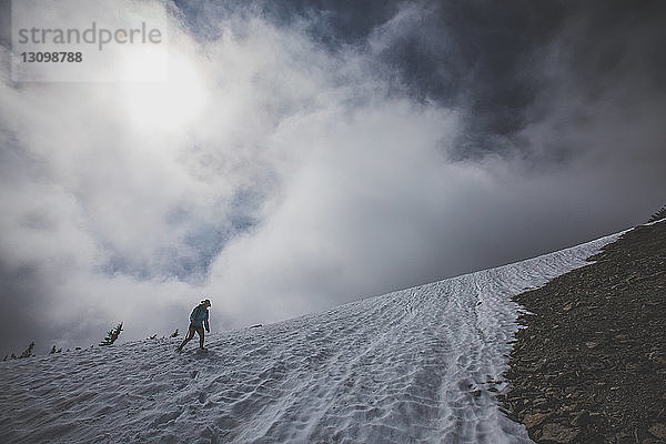 Niedrigwinkelaufnahme einer Wanderin  die auf Schnee gegen bewölkten Himmel wandert