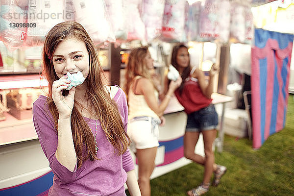 Porträt einer Teenagerin  die mit Freunden im Hintergrund Zuckerwatte isst