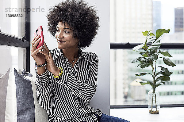 Geschäftsfrau fotografiert mit einem Smartphone  während sie im Büro sitzt